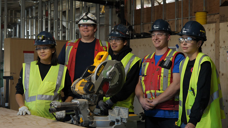 A group of 5 workers in front of a table on a construction site