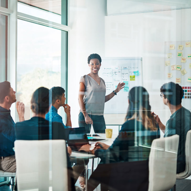 A person of color writing on a white board who is leading a meeting