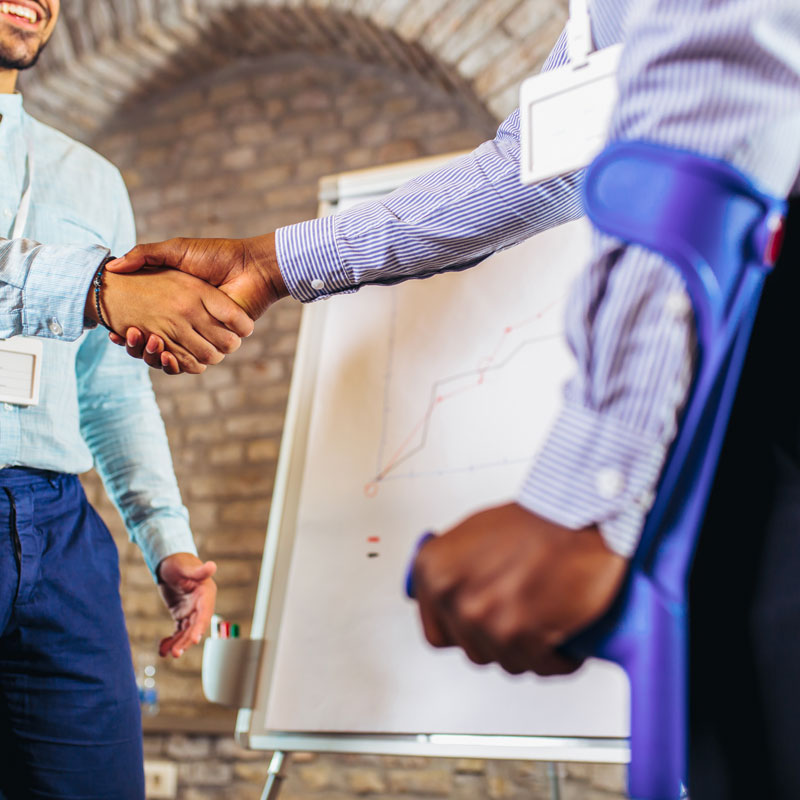 Two people shaking hands, one person is using an arm brace to stand up