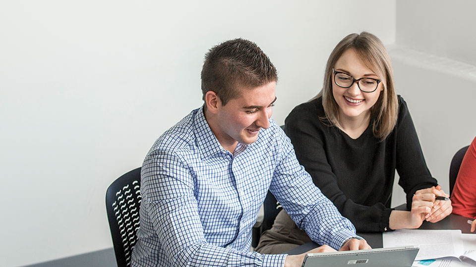 A man and a women working together with a laptop in front of them on a desk