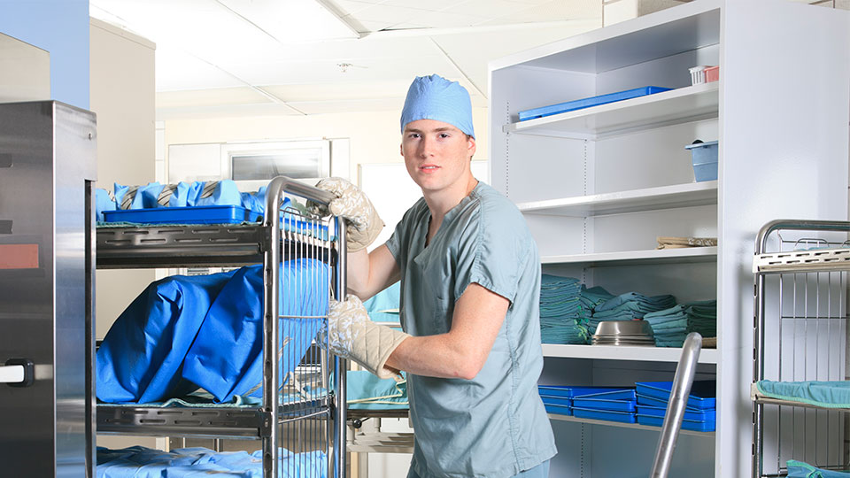 A man wearing scrubs pushing a cart of medical equipment