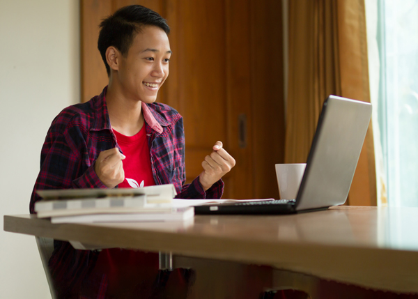 A male student celebrating his success in front of a laptop