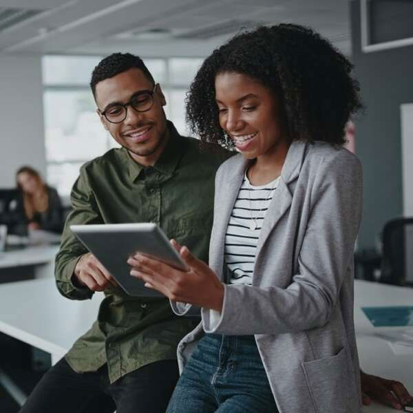 Two collegues leaning against a desk looking at a tablet