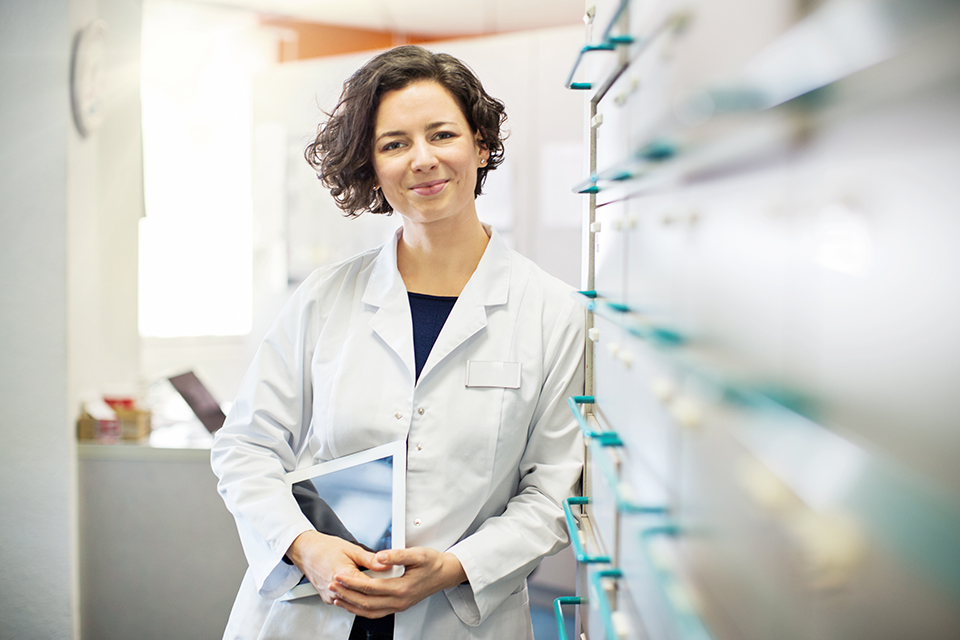 A women in a healthcare setting leaning against a set of file cabinets holding a tablet