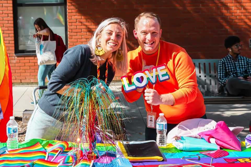 A man and a women holding a sign that says love with a rainbow border around it