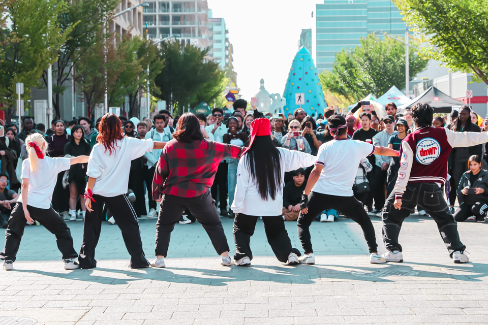 A group of performers standing in a line with their right arm straight out in front of a large crowd