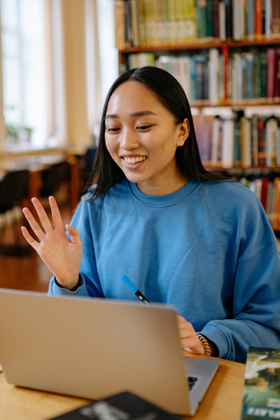 A female student sitting in front of a computer waving to it