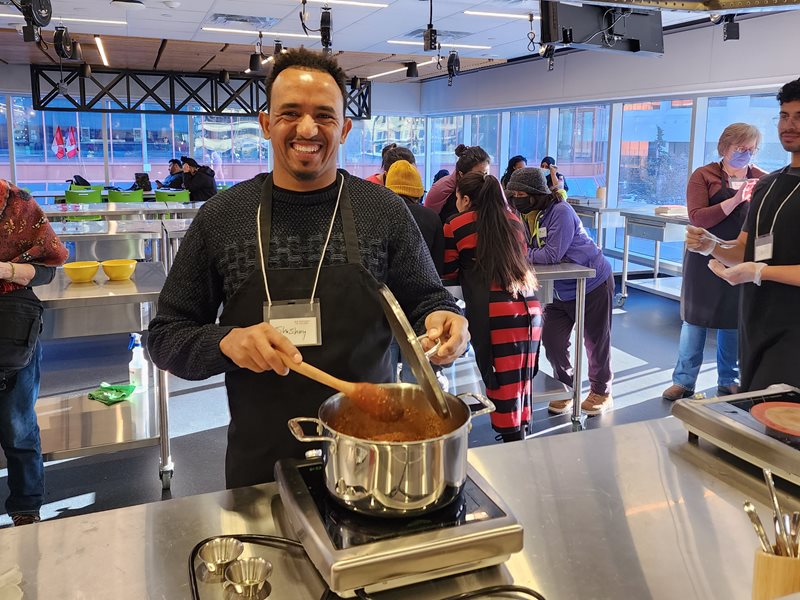 A male student stirring a pot of tomato sauce